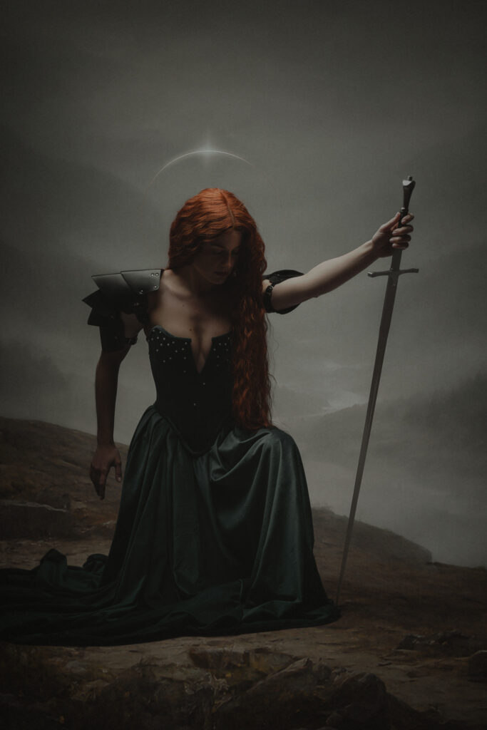 Fine art portret vrouw met rood haar, zwaard en halo knielend op bergklif — Meesterwerk Ace Photography Zaltbommel