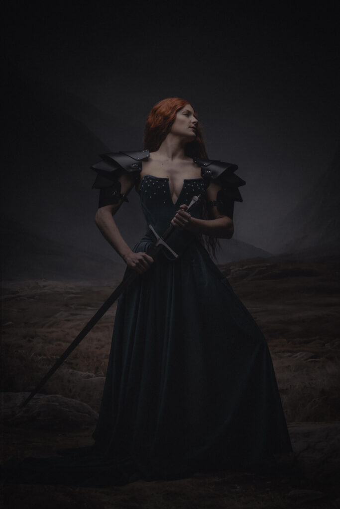 Fine art portret vrouw met rood haar, zwaard en halo knielend op bergklif — Meesterwerk Ace Photography Zaltbommel