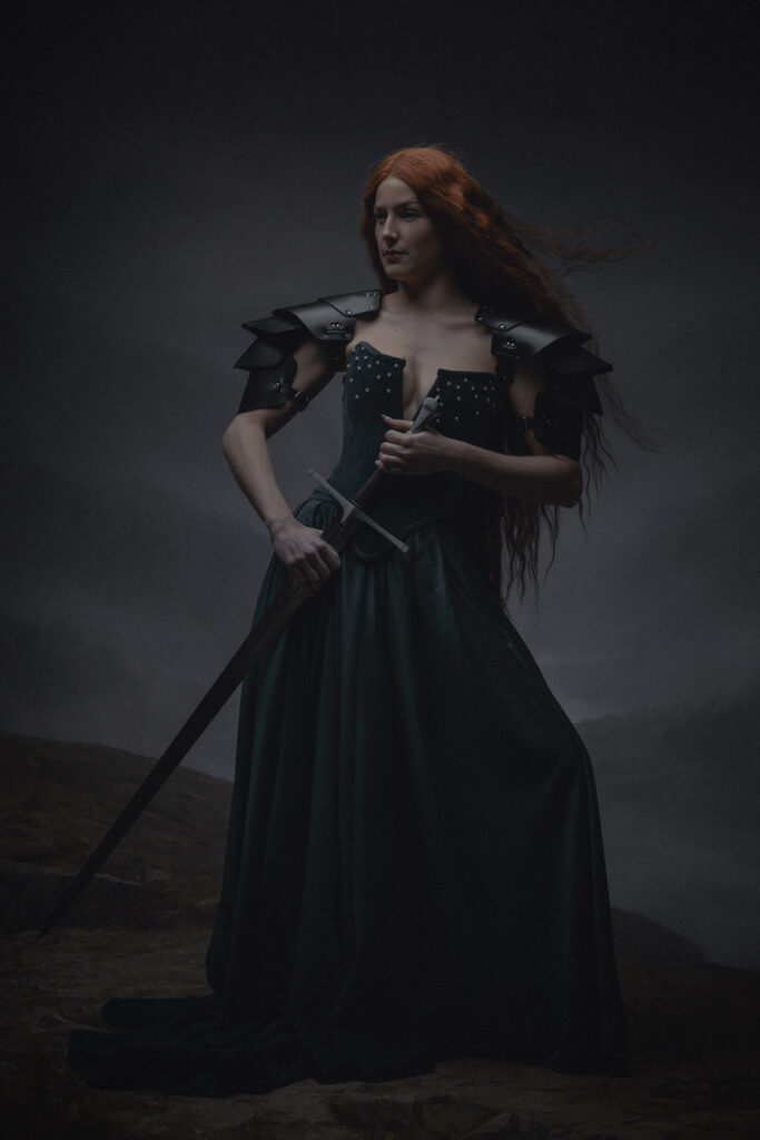 Fine art portret vrouw met rood haar, zwaard en halo knielend op bergklif — Meesterwerk Ace Photography Zaltbommel