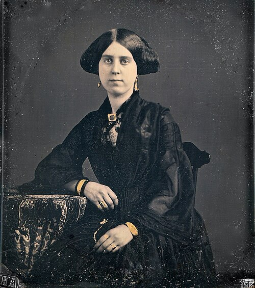 Waarom lachen mensen op een foto? Een korte geschiedenis. Negentiende-eeuws portret van een serieus kijkende vrouw in donkere kleding, een daguerreotypie Een portret uit de beginperiode van de fotografie: kalm, stil, bijna een schilderij.